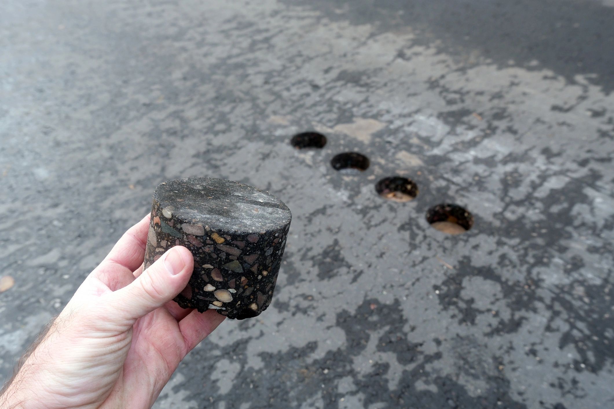 Hand holding an asphalt core sample for road testing