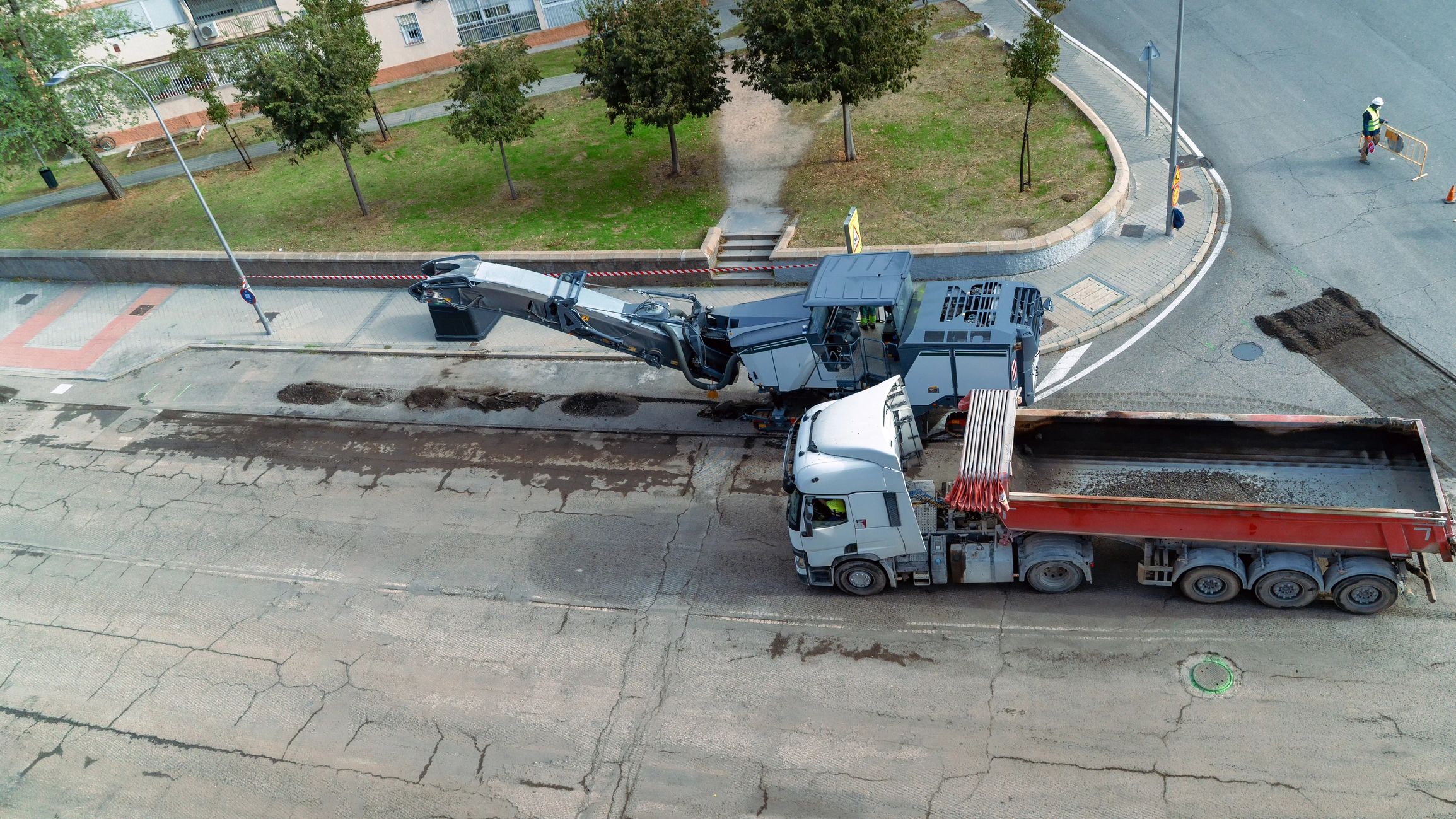 Road construction workers operating heavy machinery removing damaged asphalt surface from city street