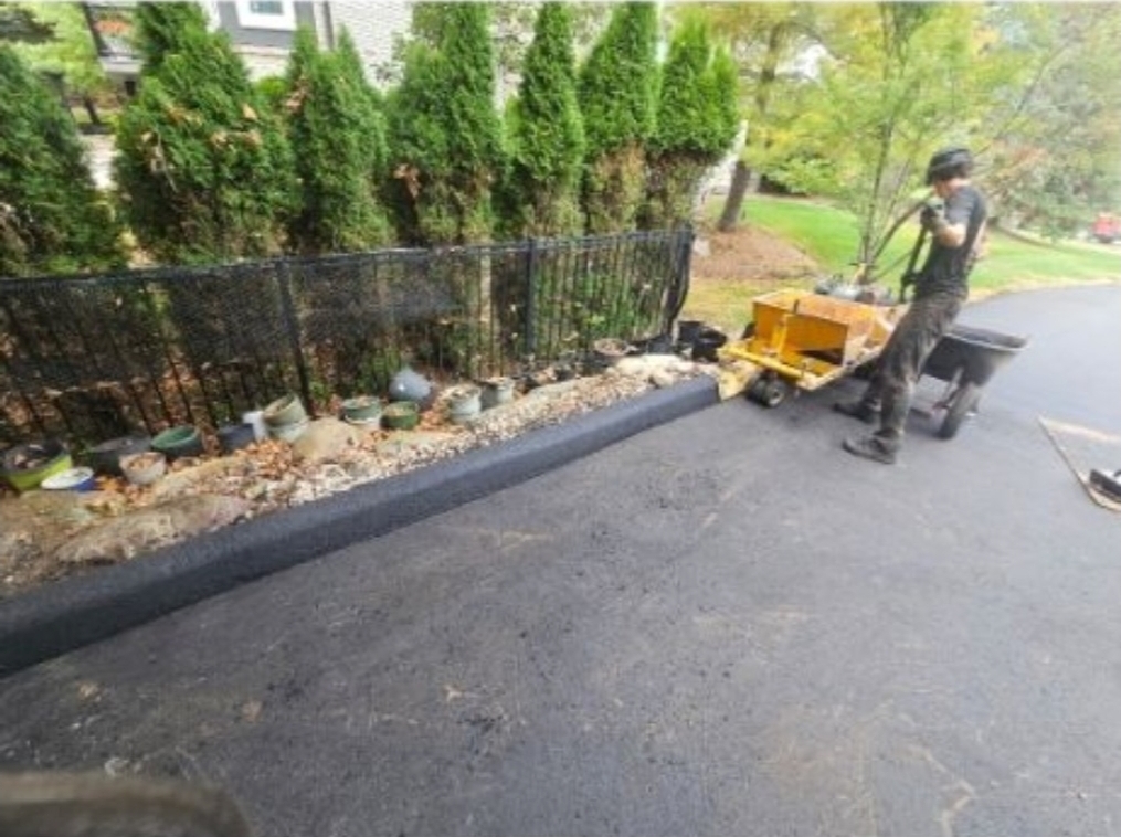 Asphalt curb installation using a curb machine along residential driveway edge.